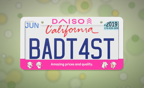 Daiso license plate frame in white and pink with the Daiso logo and "Amazing prices and quality.", front view on a soft green bokeh background
