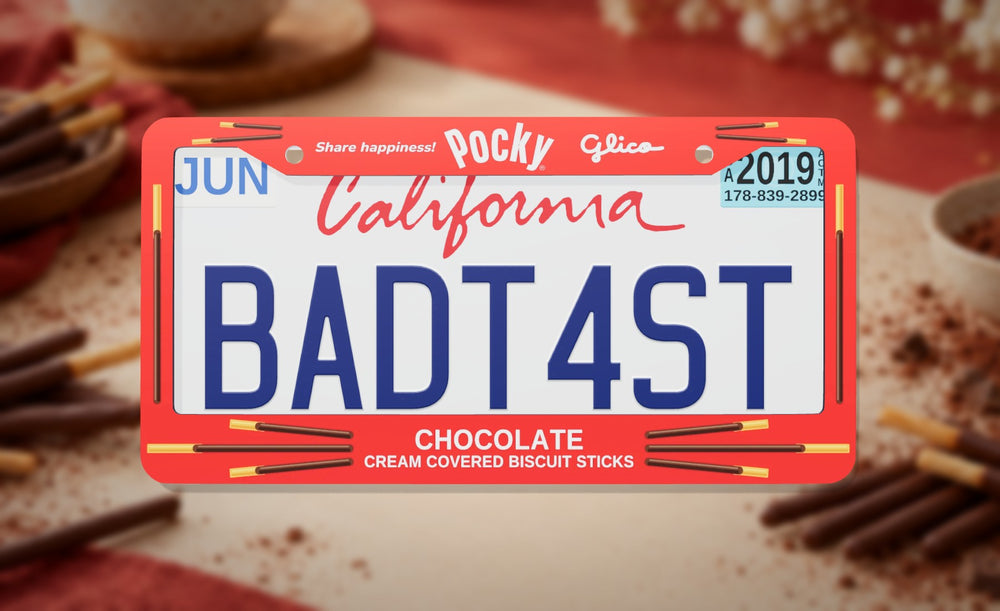 Pocky license plate frame in red with the Pocky and Glico logos and chocolate biscuit sticks, front view on a red and cream tabletop with chocolate biscuit sticks