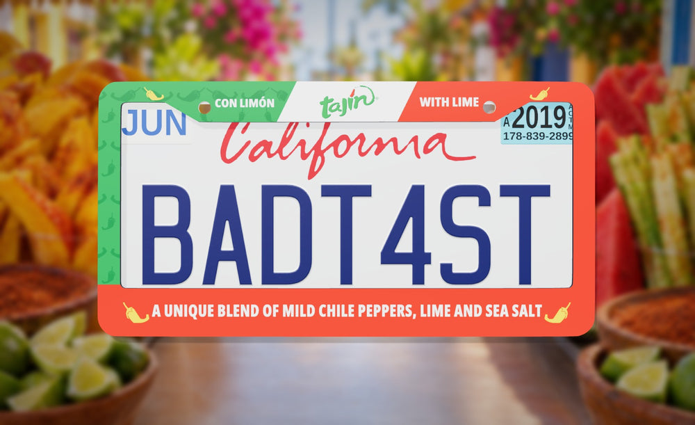 Tajín license plate frame in green and red with the Tajín logo, con limón and with lime, front view on a Mexican fruit stand background