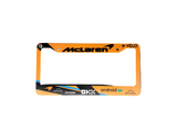 Orange and black license plate frame with various brand logos on a gray surface