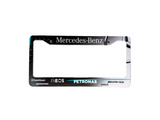 Metallic license plate frame with Mercedes-Benz, Petronas, and INEOS branding on a gray surface.