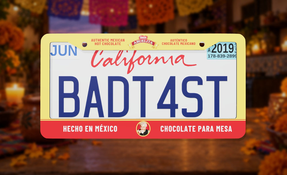Abuelita license plate frame in yellow and red with the Abuelita logo and Hecho en México, Chocolate para Mesa, front view on a candlelit Mexican kitchen background