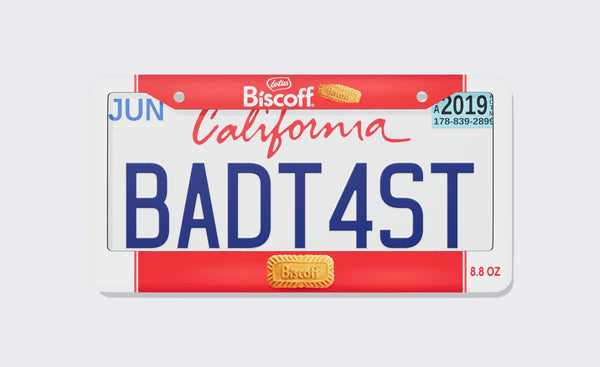 Lotus Biscoff license plate frame, front view: red package-style bands with the Lotus Biscoff logo and a cookie on top, natural-ingredients callouts and a large embossed Lotus cookie on the bottom, Net Wt 8.8 oz on the side