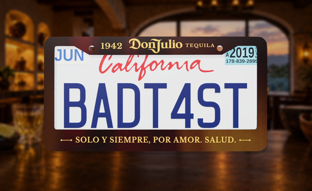 Don Julio license plate frame in dark brown with the Don Julio 1942 Tequila logo, front view on an agave hacienda bar at dusk background
