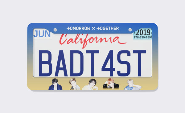 TOMORROW X TOGETHER license plate frame front view: blue-to-gold gradient frame with the white TOMORROW X TOGETHER logo on top and five member portraits along the bottom, shown on a California plate